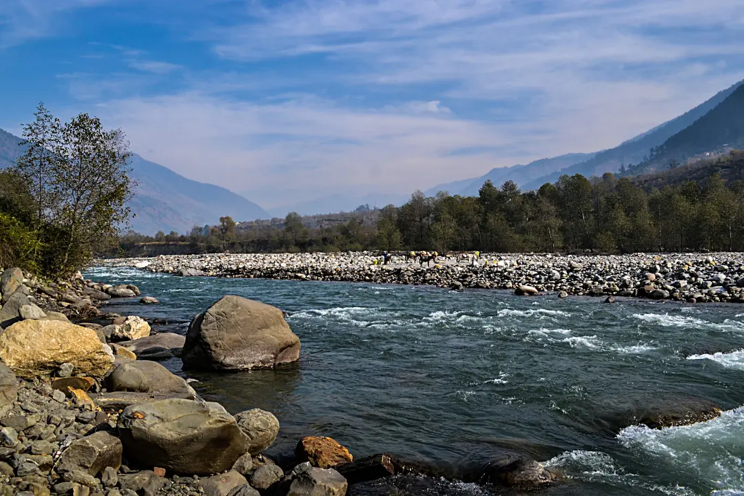 Scenic view of a river flowing through Kullu with rocks and mountains in the background